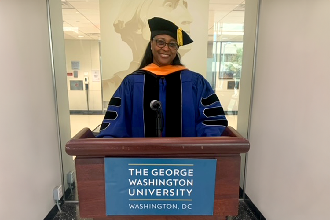 Keesha Holmes standing at podium in graduation regalia