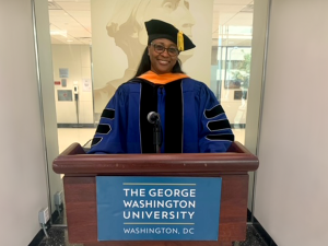 Keesha Holmes standing at podium in graduation regalia