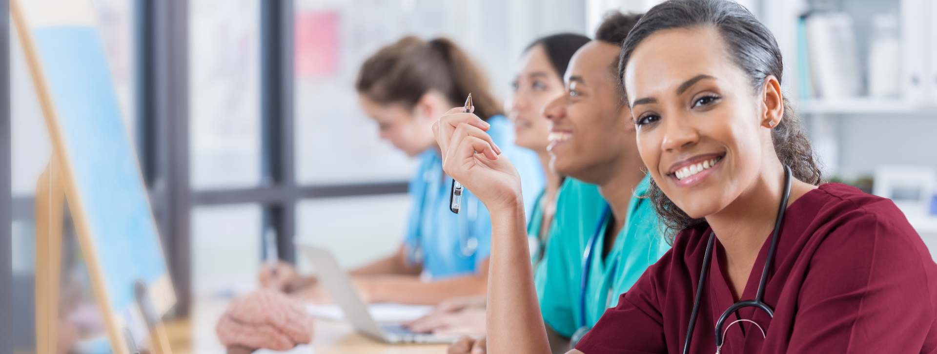 Nursing student in classroom setting, smiling at desk